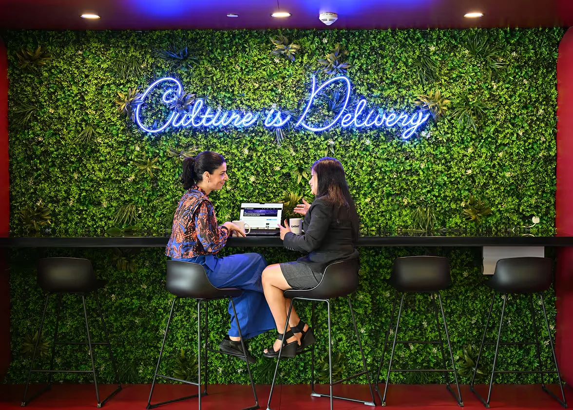 Two CNTXT colleagues talking in front of the “Culture is Delivery” wall